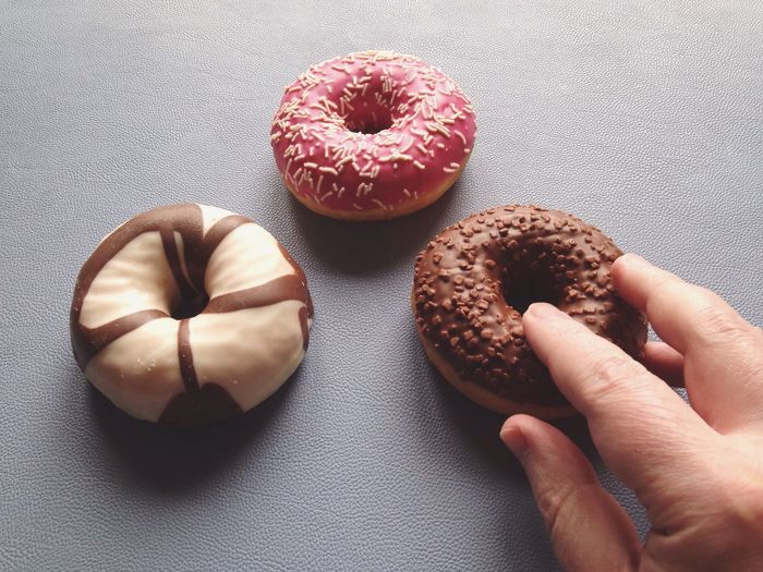 Close-up of cropped hand touching donut on table