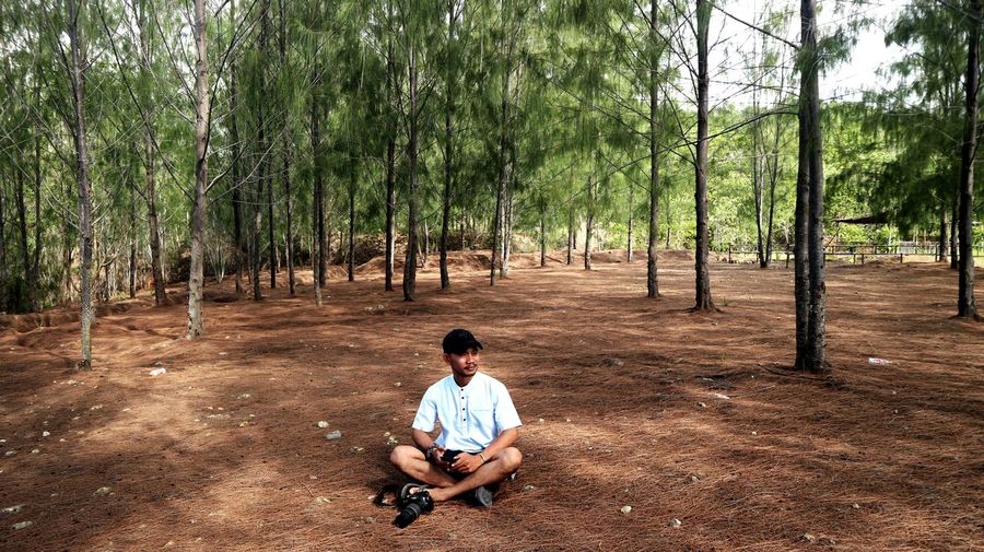 Full length of young man sitting on land in forest