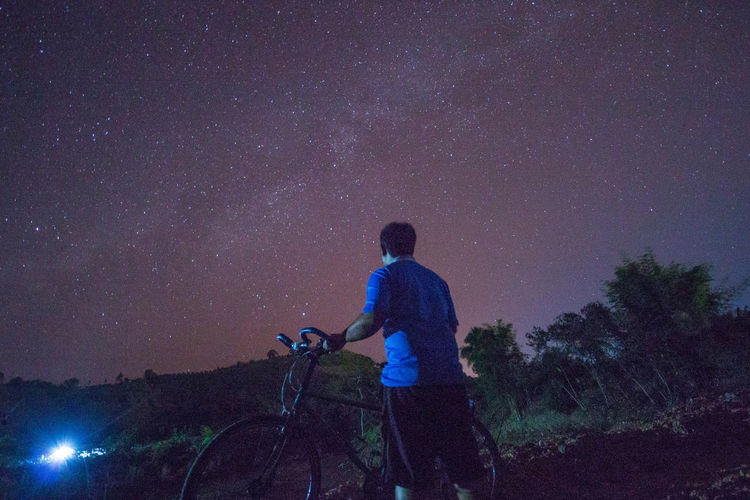 Rear view of man with bicycle against star field at night