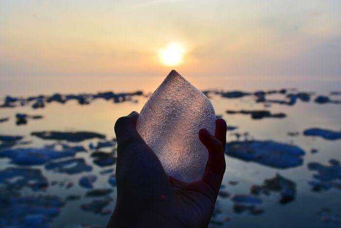 Cropped hand of person holding ice at beach during sunset