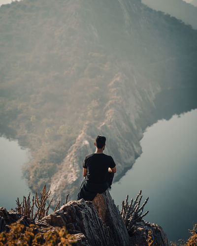 Rear view of man sitting on rock looking at mountain