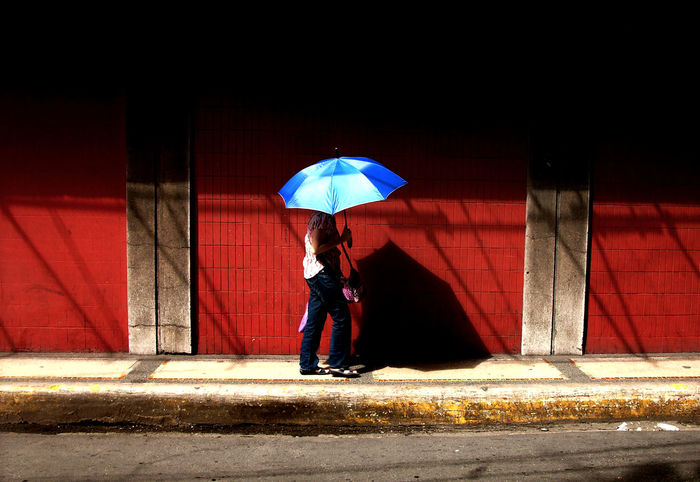 Woman with umbrella walking on footpath by wall