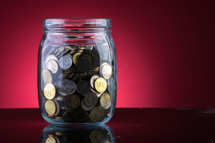 Close-up of coins in jar against red background