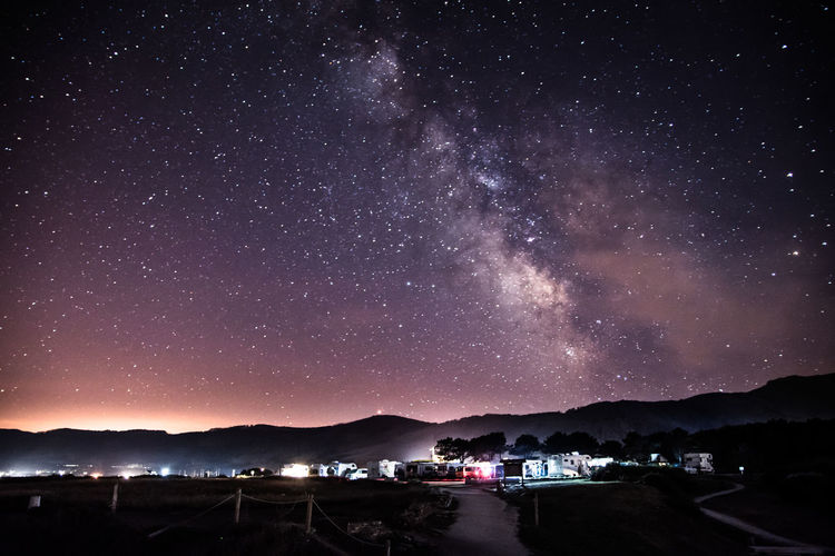 Illuminated houses by mountains against sky at night