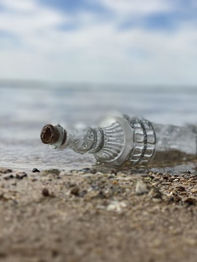 Glass bottle washing up on shore with water and sky in the back