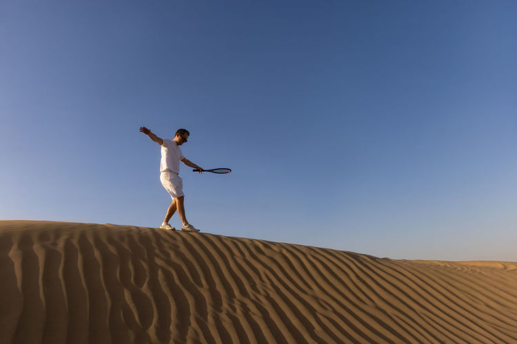 Rear view of woman jumping on sand at desert against clear sky