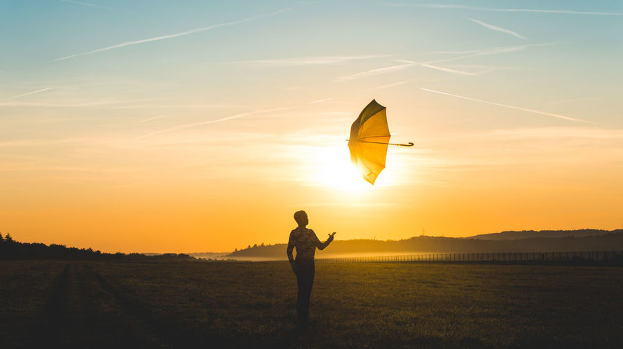 Woman throwing umbrella against sky during sunset