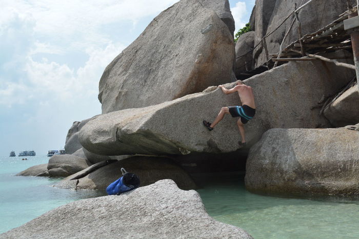 Shirtless man climbing rock on beach