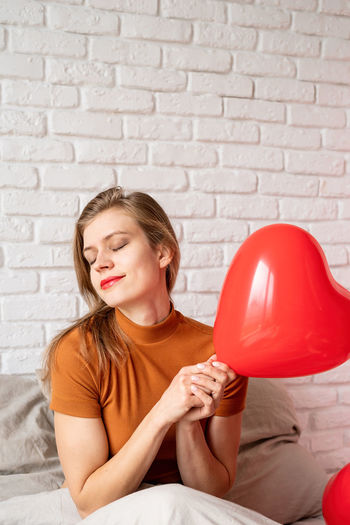 Portrait of young woman holding heart shape against wall