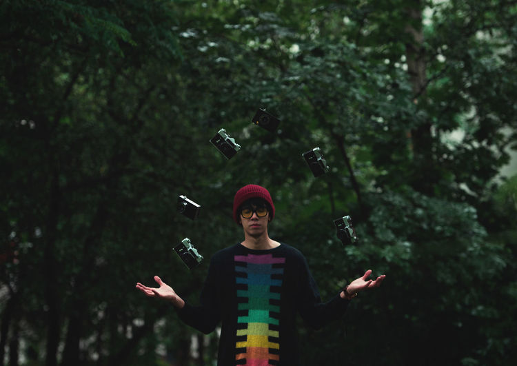 Man juggling cameras while standing against trees