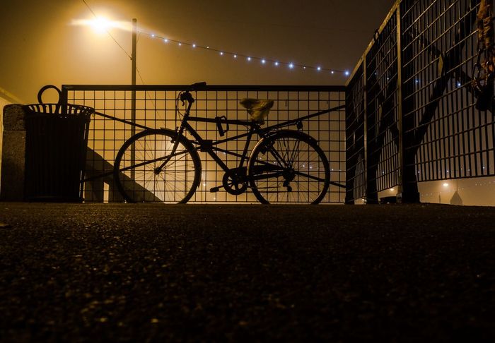 Silhouette bicycle parked against railing and sky at night