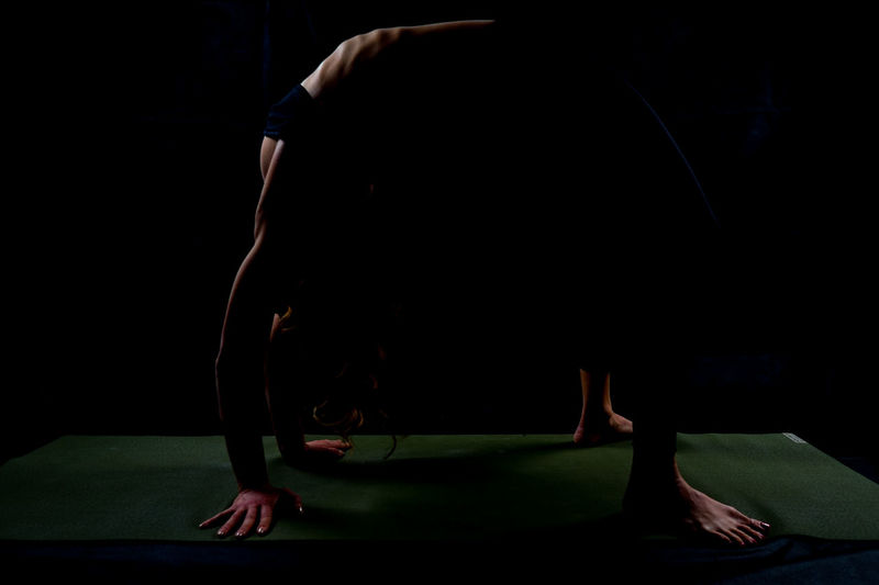 Side view of athlete bending over backwards on exercise mat against black background
