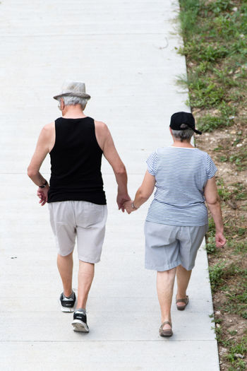 Rear view of couple holding hands while walking on footpath