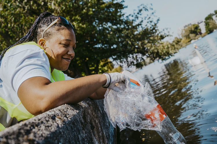 Tilt image of smiling woman picking up plastics from lake