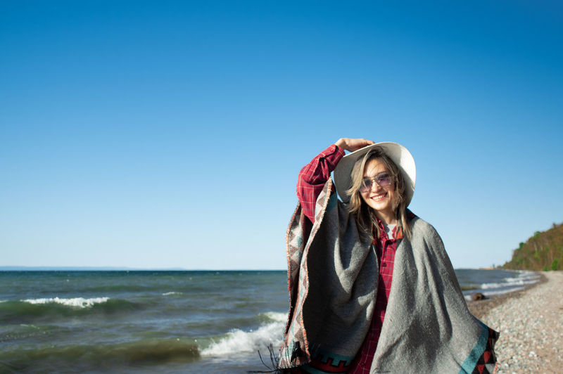 Portrait of smiling young woman on beach against clear blue sky