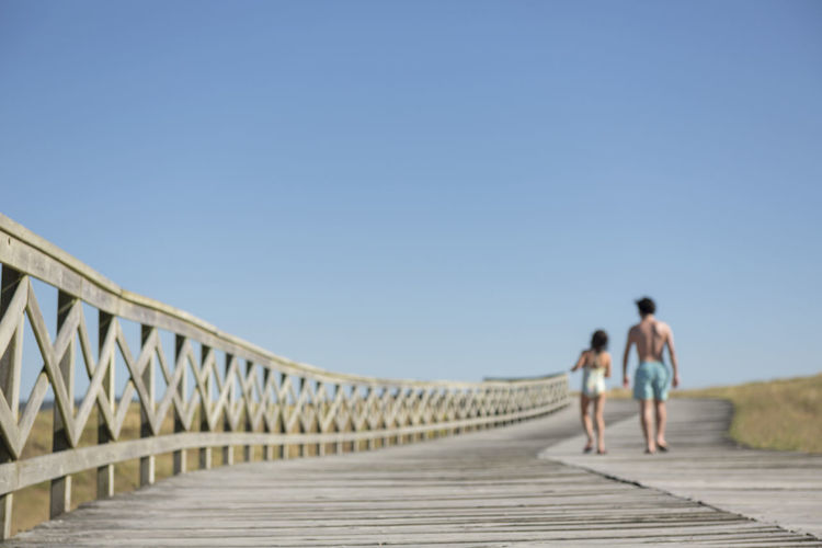 Rear view of people walking on bridge against clear sky
