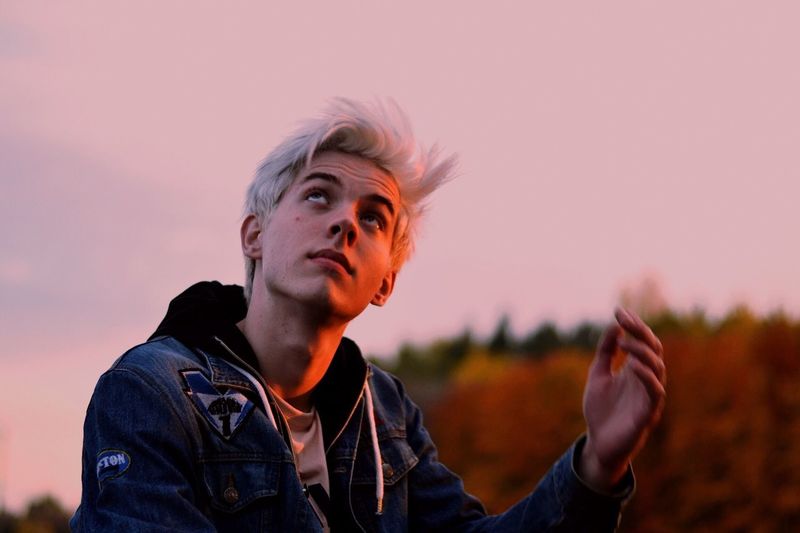 Handsome young man looking up against sky during sunset