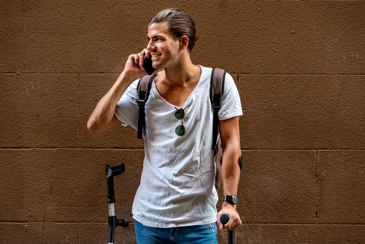 Young latin man with crutches and mobile in the street