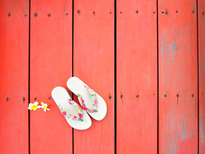Directly above shot of flowers and slippers on red floorboard