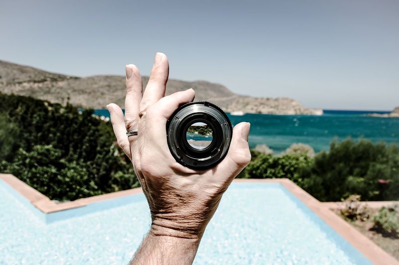 Cropped hand of person holding lens against sea
