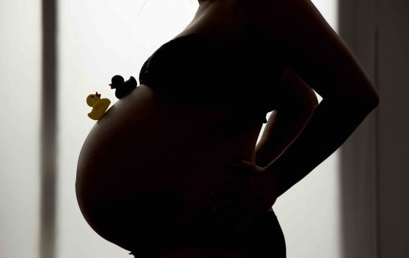 Midsection of pregnant woman with rubber ducks on belly in darkroom