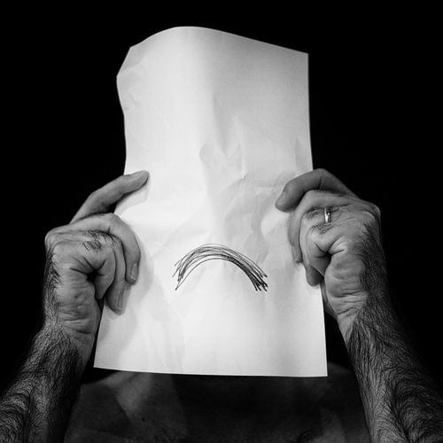 Man holding sad face in front of face against black background