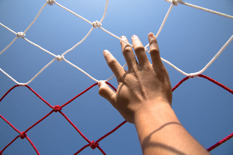 Cropped hand touching soccer net against clear sky