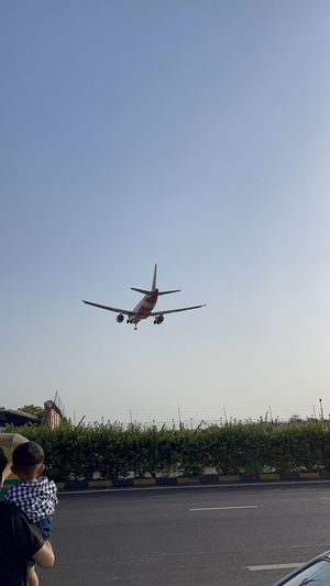 Rear view of people with airplane flying against clear sky