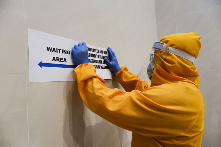 Side view of man wearing protective suit holding information sign on wall
