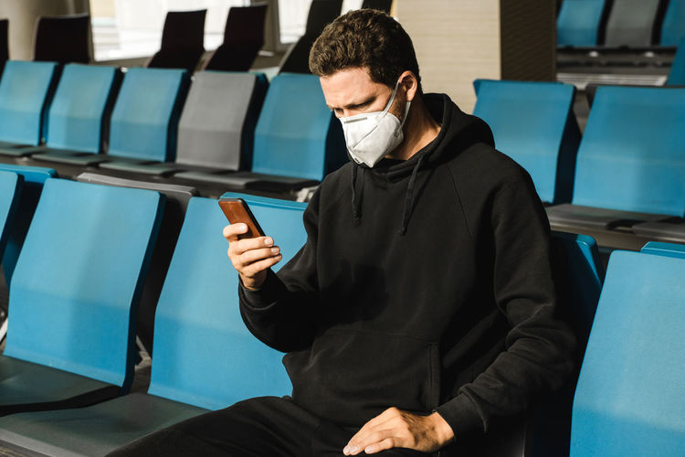 Man in respirator mask n95 is waiting next plane at the airport and using mobile phone.