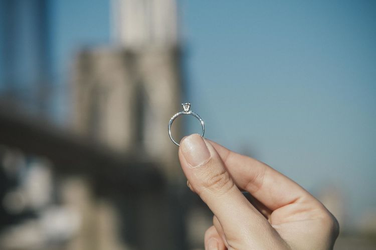 Close-up of hand holding wedding ring by brooklyn bridge
