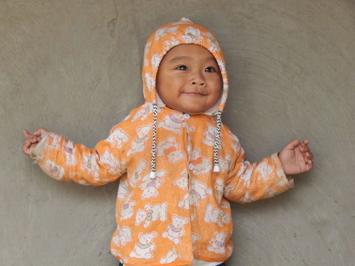 Portrait of smiling baby boy in warm clothing standing against concrete wall