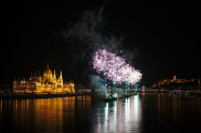Fireworks over river against sky at night
