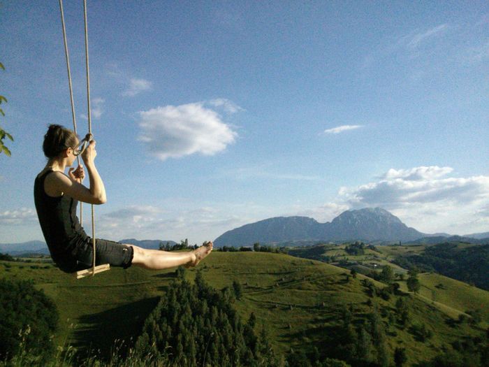 Side view of woman sitting on swing against landscape