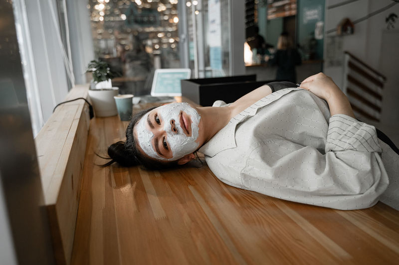 Woman with face mask lying on table at home