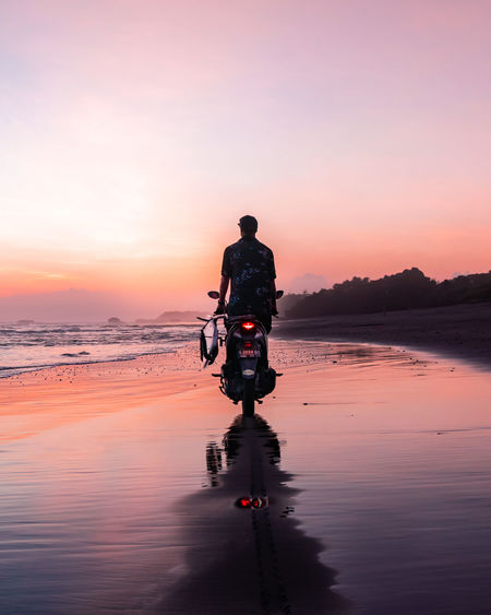 Rear view of man riding on sea against sky during sunset