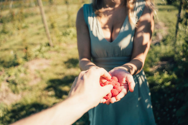 Cropped hand of friend taking raspberries from woman hand