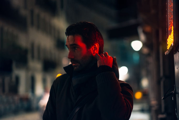 Night street portrait of a man in the city illuminated by the neon or led lights in winter