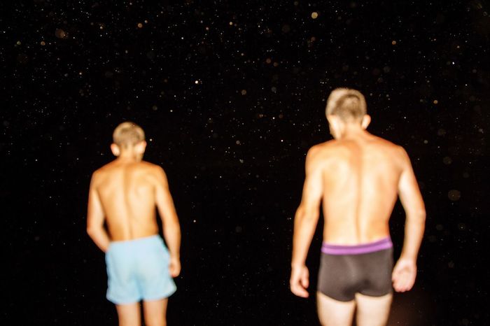 Rear view of shirtless friends standing against star field at night