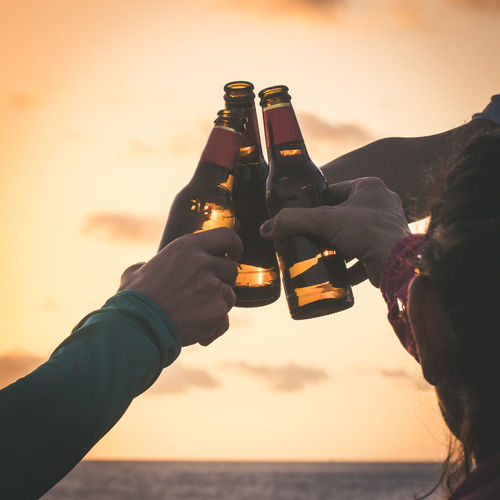 Close-up of people toasting beer against sky during sunset