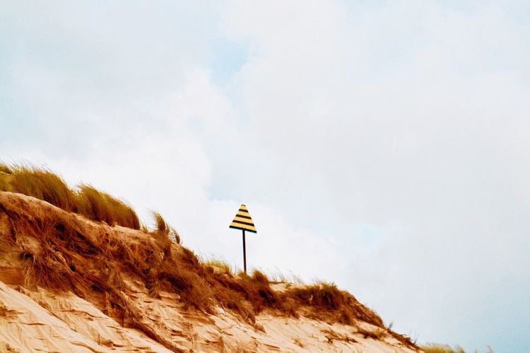 Sign on sand dune against sky