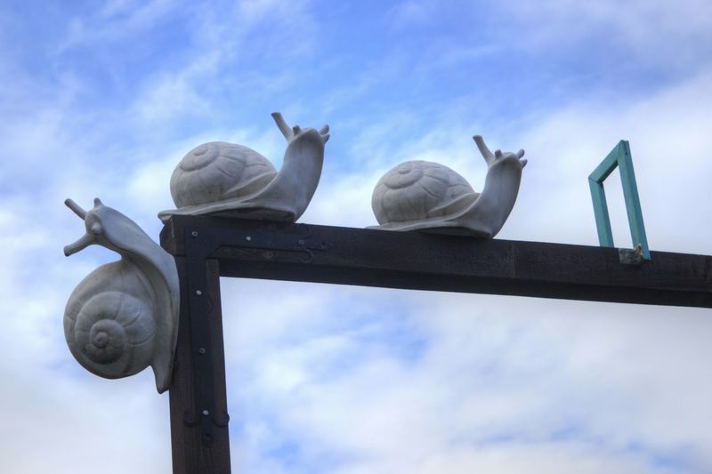 Low angle view of snail statues on structure against sky
