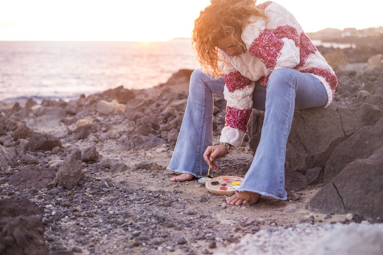 Mature woman painting pebble at shore