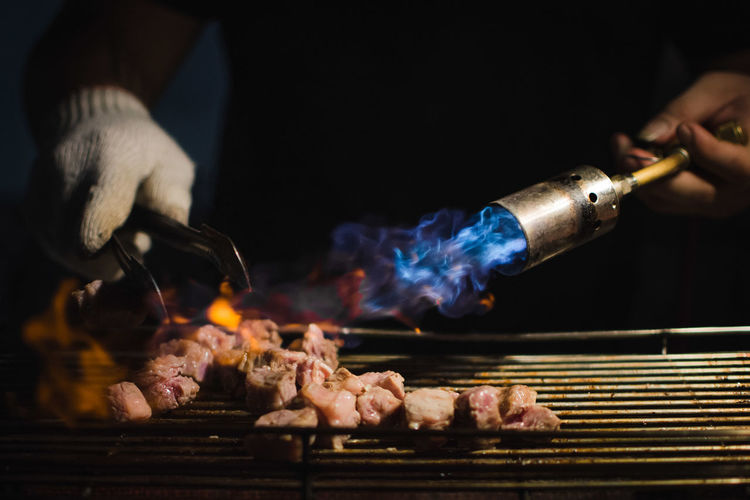 Close-up of hand preparing meat on barbecue grill
