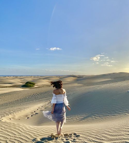 Rear view of woman walking on sand dune against sky