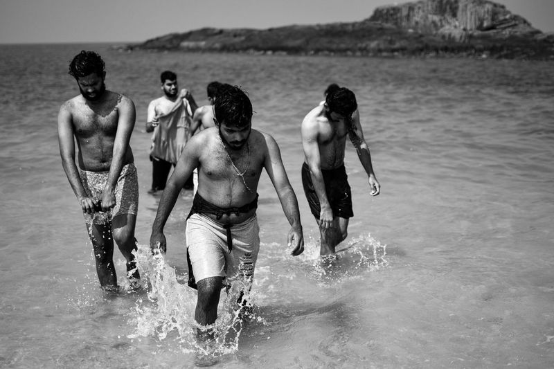 Shirtless men walking in sea