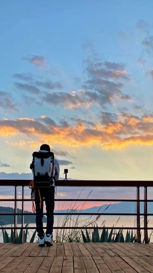 Rear view of man photographing on railing against sky