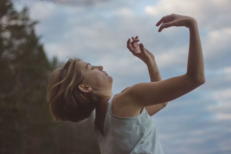 Side view of beautiful woman dancing against cloudy sky