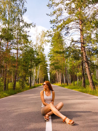Portrait of woman sitting on road amidst trees