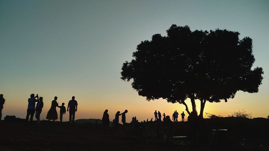 Silhouette of people standing on land against sky during sunset